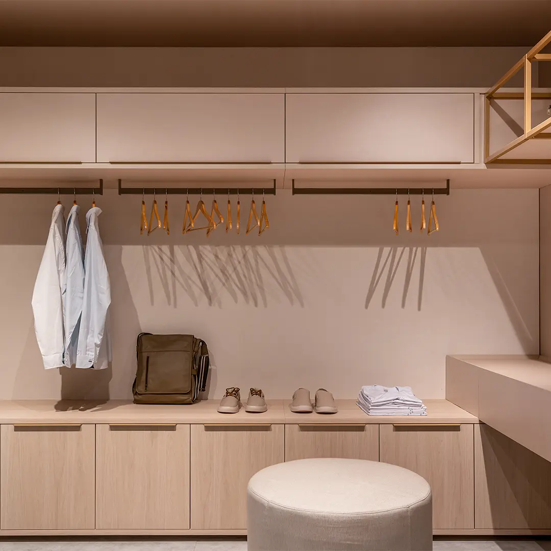 Closet planejado Italínea em madeira clara com cabideiros, armários e banco central — Dormitório planejado Italínea em Manaus